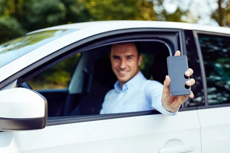 A smiling Miwayz driver showing the app from his car